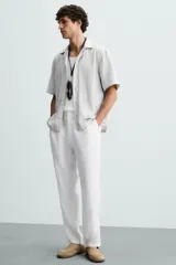 Pantalón de vestir blanco, confeccionado en lino, de corte recto, con bolsillos laterales y traseros. Se ajusta a la cintura con botón y cierre.