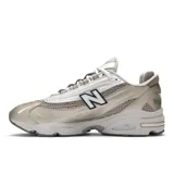 Championes New Balance modelo 1000 color plateado y beige, con detalles en negro. Diseño futurista con superposiciones de malla y ante, amortiguación ABZORB en talón y antepié, y caña Stability Web en el mediopié.