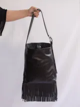 Bolso tipo bandolera de cuero negro con flecos y tachas plateadas. Tiene correa regulable, forro interior y bolsillo interno.