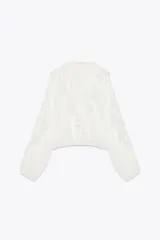 Blusa blanca de escote en pico y manga larga abullonada con elástico en los puños. Detalle de volantes en el mismo tejido.