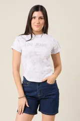 Remera blanca con estampado tie-dye en tonos grises y logo "LOU JEANS" con apliques brillantes.
