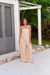 Conjunto de dos piezas color beige claro, compuesto por un top strapless con bajo asimétrico y un pantalón de tiro alto con pierna ancha y caída fluida.