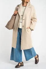 Tapado largo color beige claro, de corte oversize, con cuello solapa y cierre frontal de botones.