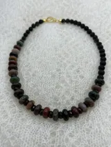 Collar corto de cuentas de piedra natural en tonos marrones, verdes y negros, con cierre de gancho dorado.