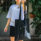 Bolso tipo tote bag negro con asas largas, bolsillo exterior con cierre y bordado con la palabra "GAINS." en blanco.