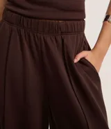 Pantalón de mujer color marrón oscuro, de tiro alto con cintura elástica fruncida y corte ancho recto. Presenta vincos delanteros marcados.