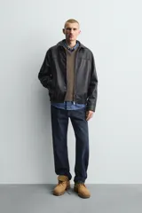 Cazadora bomber de efecto piel color marrón oscuro, con cuello solapa, cierre frontal de cremallera, bolsillos de vivo en cadera y bajo elástico.