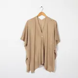 Ruana de tejido de punto color beige, con escote en V y un botón frontal. Presenta mangas cortas tipo murciélago y un calce amplio con caída asimétrica.