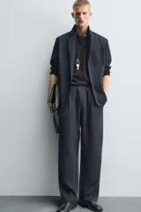 Pantalón negro de corte relajado con cintura elástica ajustable y pliegues en la parte delantera. Presenta bolsillos laterales y bolsillos traseros de parche.