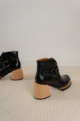 Botas cortas de cuero negro con textura tipo cocodrilo, caña alta, cierre con hebilla y taco de madera.