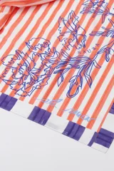 Pareo de algodón con estampado de rayas verticales naranjas y blancas, con diseño floral en azul y bloques violetas en los extremos.