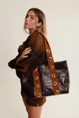 Cartera tote grande de cuero color marrón oscuro, con apliques de cuero color marrón claro y ojales metálicos dorados en las asas.