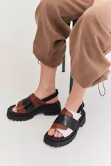 Sandalias marrones con tiras anchas de cuero texturizado y gamuza, suela track negra y hebilla ajustable en el tobillo.