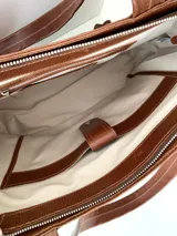 Cartera tipo tote de cuero graneado color negro, con textura uniforme y suave al tacto. Tiene manijas de 55 cm, bolsillo frontal con broche imantado, bolsillo trasero con cierre metálico, cierre principal metálico, forro interior y tres bolsillos internos (uno con cierre, uno plaqué y uno tipo sobre con solapa y botón).