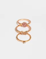 Set de tres anillos dorados con strass: uno con diseño de flor rosa, otro con diseño de mariposa y otro con una pequeña piedra verde.