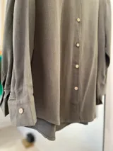 Camisa clásica verde oliva, de manga larga con cuello camisero. Cierre frontal con botones de coco y laterales con abertura.