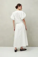 Falda midi blanca con pequeños lunares negros, de corte acampanado y cintura alta con pliegues.