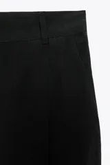 Pantalón cropped marrón de tiro medio y pierna ancha, confeccionado en hilatura con mezcla de lyocell. Presenta trabillas en la cintura, bolsillos laterales y pinzas en el delantero. Cierre frontal con cremallera y botón.