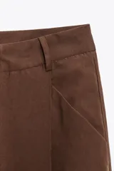 Pantalón color ladrillo de tiro medio con trabillas, detalle de pliegues, bolsillos laterales y falsos bolsillos de vivo en la espalda. Cierre frontal con cremallera y botón.