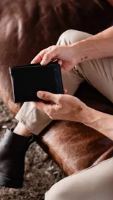 Billetera de cuero lisa color negro con pespuntes azules. Cuenta con compartimentos para billetes, visor y tarjeteros.