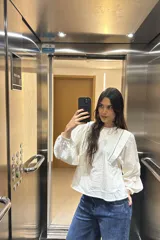Blusa blanca con textura, cuello redondo con volados y mangas largas abullonadas.