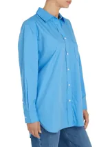 Camisa celeste de popelín de algodón orgánico, corte oversize con hombros caídos, cuello inglés, bolsillo de parche en el pecho y logo bordado en la manga.