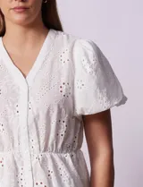 Blusa blanca de algodón con bordado broderie, escote en V con abertura central y botones, cintura elastizada y mangas cortas con terminación elastizada.