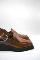 Zueco tipo mocasín color marrón con textura croco y tira regulable al talón.