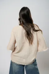Blusa beige de lino con mangas 3/4 con lazos y detalle de flecos en los puños.
