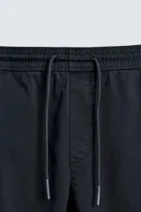 Pantalón jogger negro de corte slim fit, confeccionado en tejido de algodón con cintura elástica ajustable con cordón, bolsillos frontales y traseros de vivo, y bajo con puño elástico.