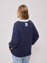 Sweater color ladrillo con cuello redondo en color crema. Estampado frontal con el texto 'Malibu Rusty' y un logo con forma de flor. Corte holgado.