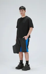 Bermuda de tela liviana de secado rápido, color negro con paneles laterales en azul eléctrico. Posee cintura elástica con cordón de ajuste estampado y bolsillos laterales y un bolsillo cargo con solapa en la pierna derecha.