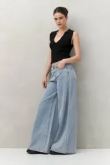 Pantalón de jean negro de corte ultra wide, tiro medio y detalles metálicos en la cintura.