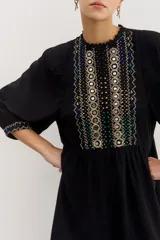 Minivestido negro de viscosa con corte en la cintura, detalles de puntillas en cuello y ruedo, gota en la espalda y pechera bordada en hilo con apliques.