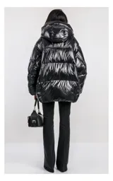 Campera oversize color blanco, confeccionada en nailon suave con un leve brillo. Cuenta con capucha, bolsillos laterales con cremallera, relleno natural y ajuste inferior con cordón. Presenta cierre frontal con cremallera de doble cursor y diseño acolchado.