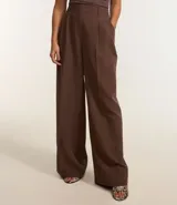 Pantalón largo de vestir color marrón chocolate, de corte sastrero con pliegues en la parte delantera y trabillas en la cintura. Confeccionado en poliéster y elastano.