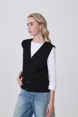 Chaleco de punto color crema, con cuello en V, cierre frontal de botones y dos bolsillos frontales.