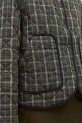 Campera capitoneada con diseño acolchado y estampado a cuadros en tonos verde oliva. Presenta un cuello de pana en color negro, cierre frontal de botones y bolsillos delanteros con ribetes oscuros.