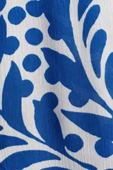 Camisa de manga corta con estampado de hojas y flores en tonos azules sobre fondo blanco. Tiene cuello clásico, botones frontales, corte holgado y canesú con pliegue en la espalda.