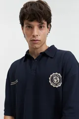 Polo azul marino con textura y corte oversize. Presenta un logo estampado en el pecho y mangas cortas.