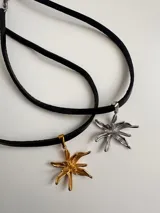 Gargantilla negra de tiento de cuero natural con dije de acero quirúrgico hipoalergénico en forma de flor.