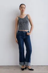 Pantalón de jean azul oscuro con corte acampanado, tiro medio y dobladillo en el ruedo. Presenta costuras marcadas en el frente y estampado abstracto en tonos grises y blancos en el interior del dobladillo.