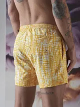 Short de baño verde con estampado de margaritas blancas y cordón ajustable naranja.