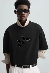 Camiseta negra de corte holgado, cuello redondo y manga corta. Estampado frontal con diseño abstracto en color blanco.