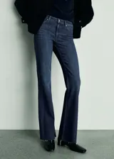 Pantalón de jean acampanado de tiro medio, color azul oscuro, con cinco bolsillos y cierre frontal con cremallera y botón.