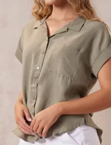 Camisa verde oliva de manga corta con cuello con solapa y abertura central con botones. Tiene un bolsillo aplicado en el pecho.