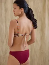 Top de bikini deportivo con estampado abstracto en tonos naranja, marrón y beige. Tiene tirantes finos con diseño a rayas verticales de colores.