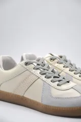 Zapatillas urbanas de cuero color crema con detalles en gris y suela de goma marrón.