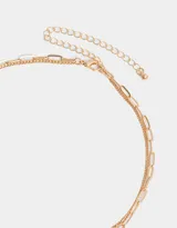 Collar corto dorado de doble cadena, una de eslabones y otra de cuentas de colores. Incluye un dije dorado con forma de sol y un dije azul con una figura grabada.
