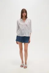 Camisa blanca de algodón con rayas verticales en tono beige/tostado y detalles de bordado tipo ojal a lo largo de las rayas. Presenta cuello mao con abertura en V y botones frontales, y mangas 3/4 con ligero volumen.